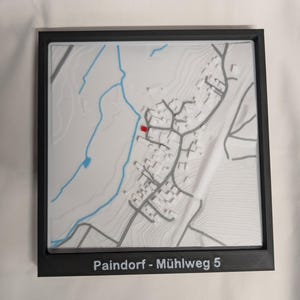 Könnte beinhalten: Eine 3D-gedruckte topografische Karte von Paindorf-Mühlweg 5, mit einem weißen und grauen Relief, blauen Wasserläufen und einer roten Markierung. Die Karte ist in einem schwarzen Rahmen, mit der Adresse unten gedruckt.