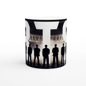 Könnte beinhalten: Weiße Keramik-Kaffeetasse mit einem Schwarz-Weiß-Design. Das Design zeigt das Wort "OTO" in großen weißen Buchstaben, mit einer Silhouette von Personen vor einem Gebäude.