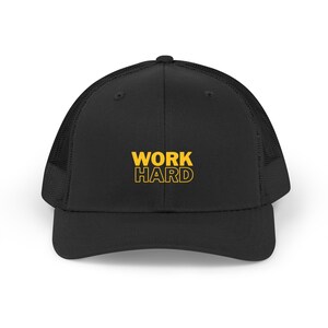 May include: Black trucker hat with a mesh back and a curved brim. The front of the hat features the words "WORK HARD" in bold, yellow lettering. This hat is a stylish accessory for casual wear.