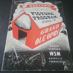 May include: Souvenir Picture Program cover featuring a red barn illustration with the words "Grand Ole Opry" in white. The cover also includes illustrations of musical instruments and the text "Radio Station WSM Nashville Tennessee."