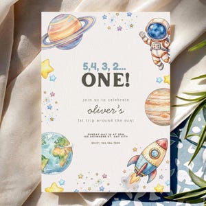 Może przedstawiać: Jasne zaproszenie z motywem kosmicznym. Zawiera ilustracje planet, gwiazd, rakiety i astronauty. Tekst brzmi "5, 4, 3, 2... ONE!" i zaprasza gości do świętowania "1. podróży Olivera wokół słońca!"