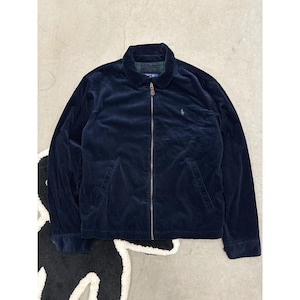 May include: A navy blue corduroy jacket featuring a full-length front zipper, a classic collar, and two side pockets. The chest displays a small embroidered green logo. The interior is lined with a dark green and navy blue plaid fabric pattern.