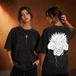 Puede incluir: Una camiseta negra con efecto lavado al ácido que presenta un pequeño gráfico blanco en el pecho con una forma geométrica y texto japonés. La parte posterior muestra una gran ilustración detallada en líneas blancas de un personaje.