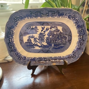 May include: A rectangular ceramic serving platter featuring a classic blue and white willow pattern. The central design depicts a landscape with pagodas, trees, and birds, surrounded by a decorative border with geometric and floral motifs.