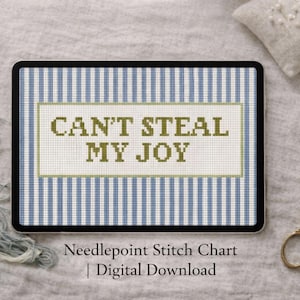 May include: A digital needlepoint stitch chart with the text "CAN'T STEAL MY JOY" displayed on a tablet. The tablet has a blue and white striped background. A pair of gold scissors and embroidery floss are also visible.