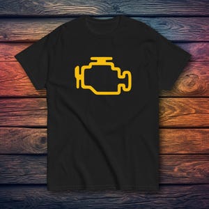 May include: Black t-shirt with a yellow engine symbol, the check engine light. The graphic is a simple outline of an engine. The shirt is made of a soft material and is suitable for casual wear. The t-shirt is a classic crew neck.