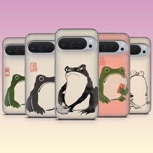 May include: A collection of phone cases featuring frog illustrations in a Japanese art style. Each case displays a different frog design in black, green, and white, with some holding objects or using a phone. The cases have a clear, protective design.