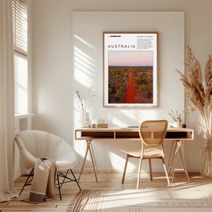 May include: A framed wall art print titled AUSTRALIA featuring a landscape photograph of a red dirt road cutting through green trees under a soft pink sky. The print includes geographic coordinates and descriptive text in black font.