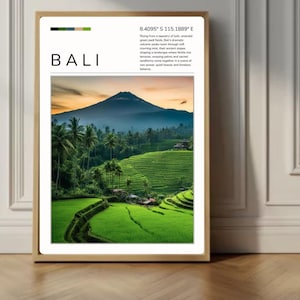 May include: A rectangular wall art print in a light wood frame featuring a photograph of Bali. The print displays the word BALI, geographic coordinates, and a descriptive paragraph above a landscape of green rice terraces and a distant volcano.