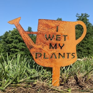 May include: A rusty metal garden stake shaped like a watering can with the words "I WET MY PLANTS" on it.