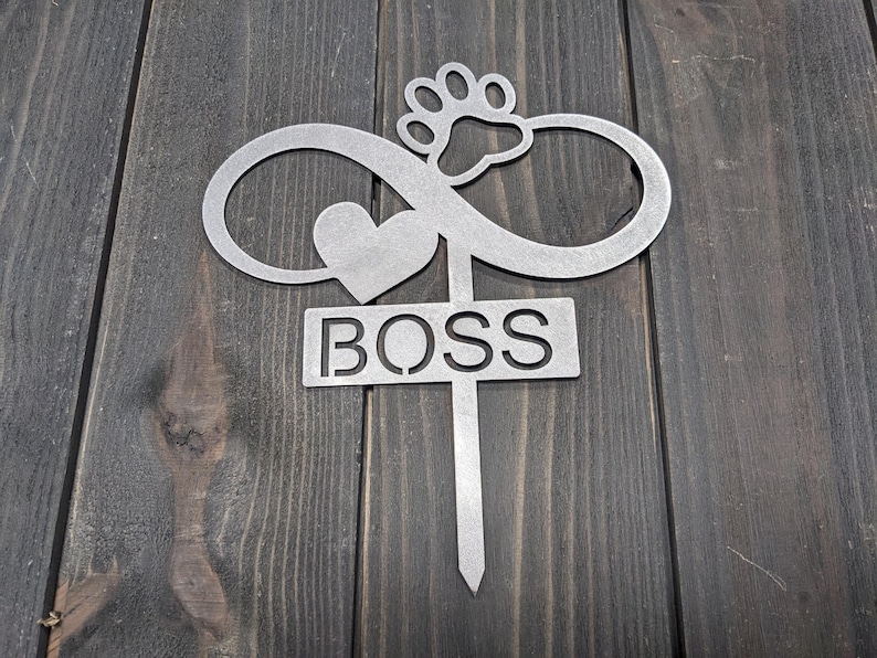 May include: A silver metal garden stake with an infinity symbol, heart, and paw print design. The word "BOSS" is cut out on a rectangular sign. The stake is designed for outdoor use.