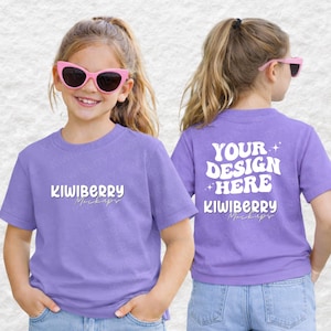 May include: Two young girls wearing matching lavender t-shirts and pink sunglasses. The front of the shirt has the text "KIWIBERRY Mockups" in white. The back of the shirt has the text "YOUR DESIGN HERE" and "KIWIBERRY Mockups".