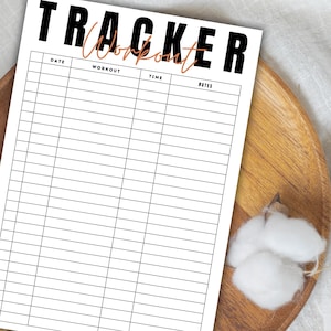 May include: A white workout tracker sheet with black and orange text. The word "TRACKER" is in large black letters, with "Workout" in orange script below. The sheet has sections for date, workout, time, and notes. The tracker is on a wooden tray.