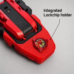 May include: A red and black Beyblade X launcher featuring an integrated lockchip holder. The device has a textured red plastic body with a circular emblem displaying a stylised flame graphic. The text BEYBLADE X LAUNCHER is visible on the side.