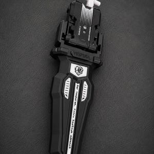 Puede incluir: Lanzador Beyblade X en blanco y negro con el texto "VESPERA" y "Beyblade X". El lanzador tiene un asa blanca en forma de cruz y un dise&ntilde;o detallado.