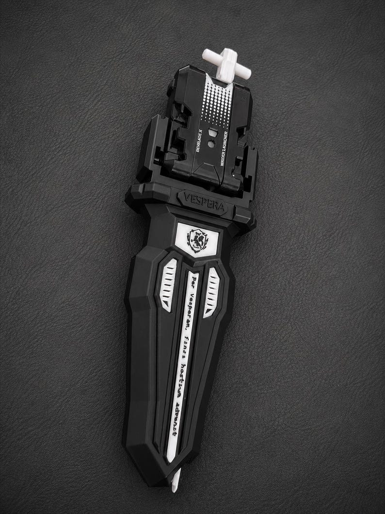 Puede incluir: Lanzador Beyblade X en blanco y negro con el texto "VESPERA" y "Beyblade X". El lanzador tiene un asa blanca en forma de cruz y un dise&ntilde;o detallado.