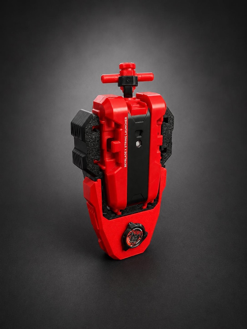 May include: A red and black Beyblade X string launcher featuring a vertical handle at the top and a circular emblem at the bottom. The central black panel is printed with the text BEYBLADE X STRING LAUNCHER in white capital letters.