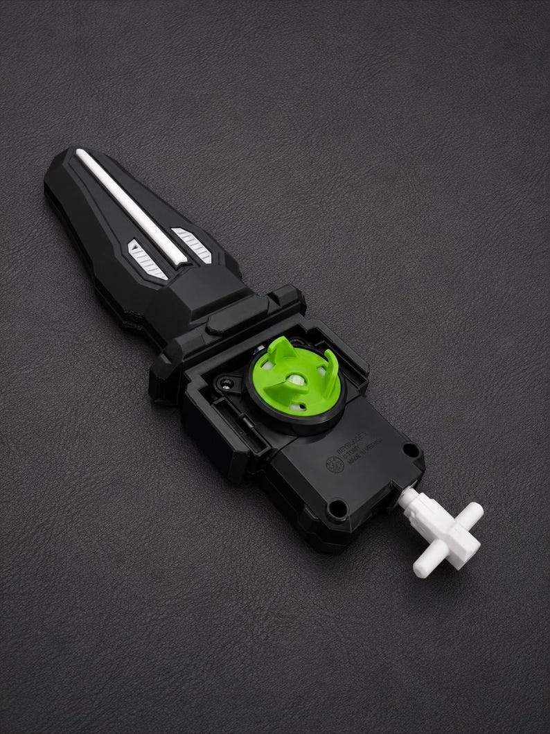Puede incluir: Lanzador de juguete negro y verde con un cord&oacute;n blanco. El lanzador tiene un mango negro con detalles plateados y un componente circular verde. El juguete est&aacute; dise&ntilde;ado para lanzar una peonza.