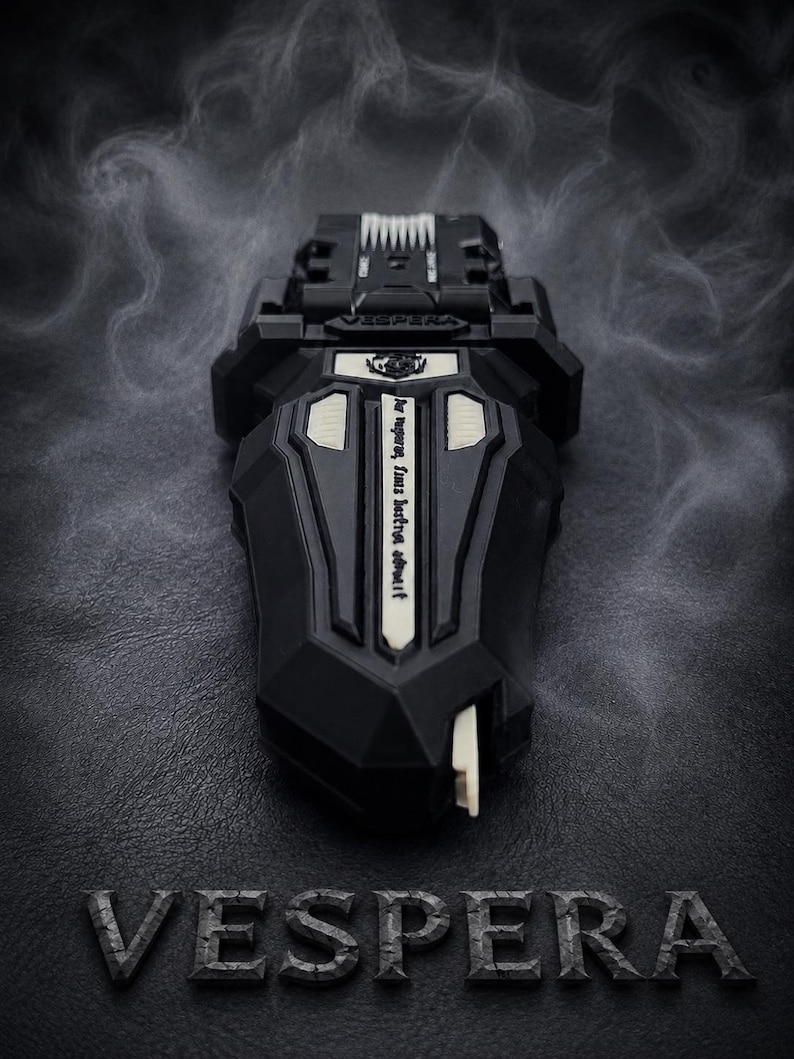 Puede incluir: Un dispositivo negro y geom&eacute;trico con detalles blancos y la palabra "VESPERA" en la parte inferior. El dispositivo tiene un dise&ntilde;o complejo con una superficie texturizada y una peque&ntilde;a palanca blanca. El fondo es oscuro con un efecto ahumado.