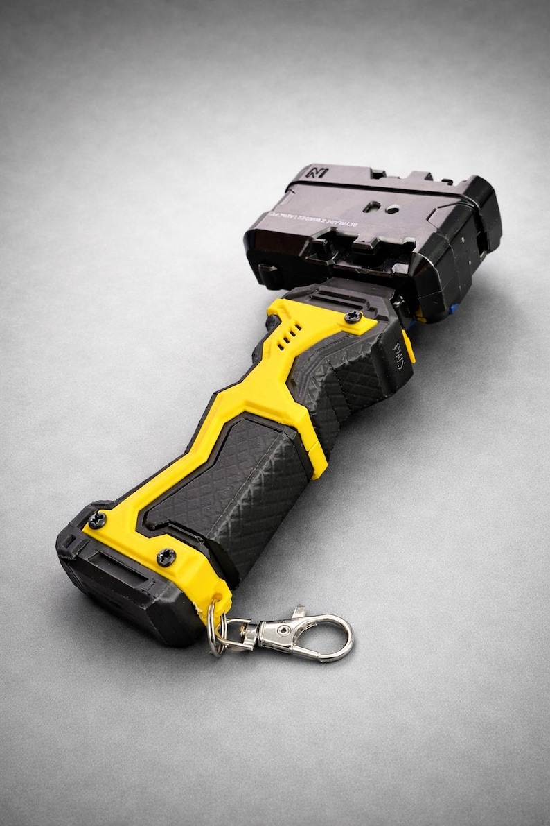 Puede incluir: Un dispositivo port&aacute;til negro y amarillo con un agarre texturizado y un cierre met&aacute;lico. El dispositivo tiene una secci&oacute;n superior rectangular y un dise&ntilde;o de acento amarillo. El dise&ntilde;o general es moderno e industrial.