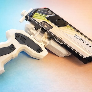 May include: A white and black toy gun with the text "BEYBLADE X". The toy has a white handle and a black and white top with green accents. The toy is designed for children.