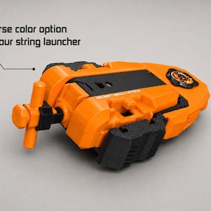 May include: An orange and black string launcher with a T-shaped handle and a circular gear mechanism. The device features the text "Diverse color option for your string launcher" and "BEYBLADE X STRING LAUNCHER" printed on the orange plastic casing.