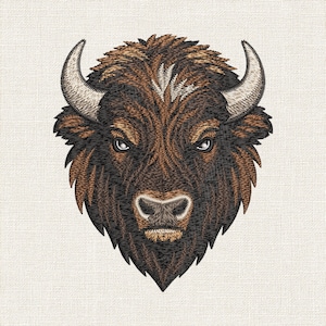 May include: An embroidered patch featuring the head of a bison in shades of dark brown, tan, and black. The design displays a detailed face with sharp eyes, a textured snout, and two curved, light-colored horns against a neutral fabric background.