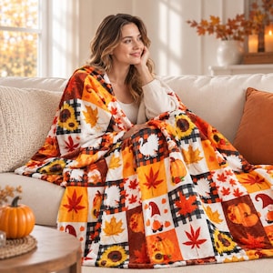 Puede incluir: Una manta de felpa con un diseño de patchwork de cuadrados con temática otoñal. El patrón incluye ilustraciones de calabazas naranjas, girasoles amarillos, hojas de arce rojas, pavos blancos y gnomos sobre un fondo de cuadros negros y blancos.