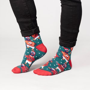 May include: A pair of festive socks with a teal background and a pattern of penguins wearing Santa hats and sweaters. The socks have red heels and toes, and white snowflakes are scattered across the design.