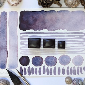 May include: Watercolour swatch card in shades of purple and lavender. The card displays brush stroke samples, geometric shapes, and three dark square objects. The artist's name, Camber Vic, is visible in the bottom left corner.