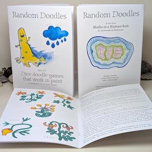 Può includere: Sono esposti due libri aperti intitolati "Random Doodles". La prima copertina presenta una creatura gialla simile a un dinosauro con accenti blu e il testo "Dice doodle-games that work in paint". La seconda copertina ha un design astratto colorato.