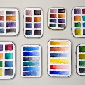 May include: Assortment of watercolor paint sets in metal tins. Each tin contains a variety of colors, including blues, greens, reds, and yellows. The tins are labeled with the names of the colors.