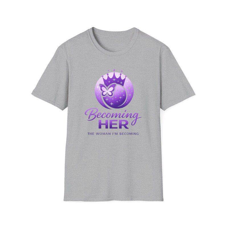 May include: A gray t-shirt featuring a purple graphic with a crown, butterfly, and the words "Becoming Her" and "The Woman I'm Becoming". The design is centered on the front of the short-sleeved shirt.