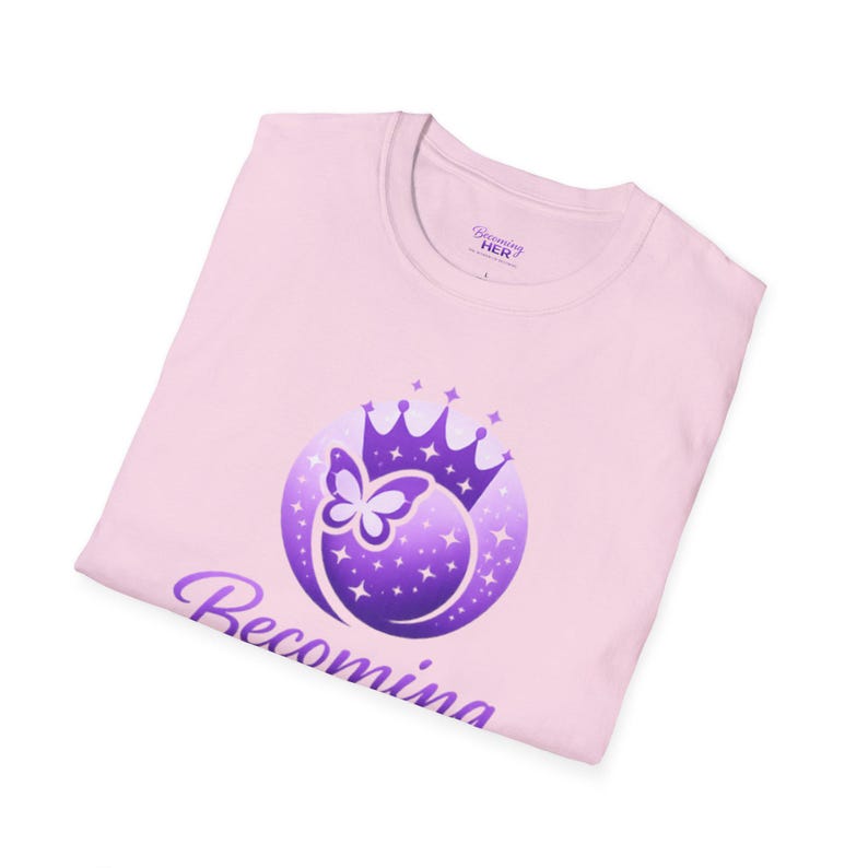 May include: A light pink t-shirt with a purple graphic featuring a butterfly inside a crown, surrounded by stars. The word "Becoming" is printed in purple script below the graphic. The brand name "Becoming HER" is printed on the tag.