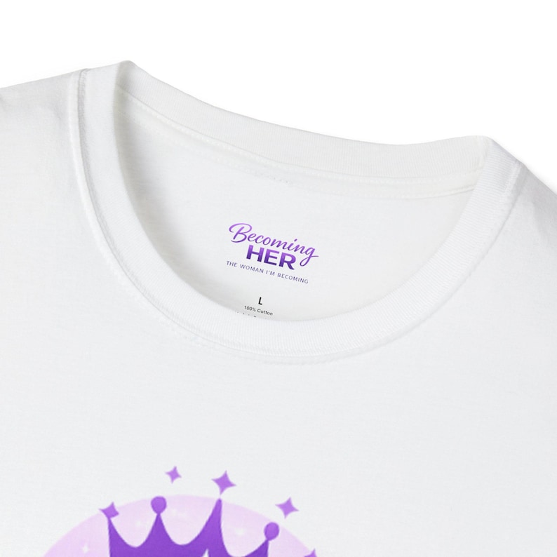 May include: White crew neck t-shirt with the text "Becoming HER" in purple script. The shirt also features the text "THE WOMAN I'M BECOMING" and a size "L" label. Made of 100% cotton.