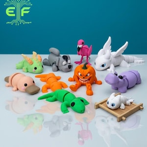 May include: A collection of colorful, whimsical figurines. The assortment includes a green lizard, a pink flamingo, a purple hippo, a white dragon, and a smiling orange pumpkin. Other figures include a platypus and a gray dog.