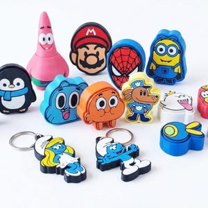 May include: A collection of colorful character keychains, including a pink starfish, a penguin with a scarf, and a blue Minion. The keychains feature various cartoon and comic book characters, perfect for fans of pop culture.