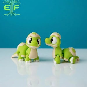 May include: Two green and tan cartoon turtle figurines with large black eyes and white highlights. The turtles are on a reflective surface against a teal background. The logo "EF" is in the top left corner.