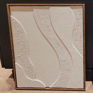 May include: Abstract white textured art piece with a wooden frame. The artwork features flowing, curved shapes with varying textures. The frame is a warm, natural wood tone. The text at the bottom reads: Frame not included and shown for styling purposes only.