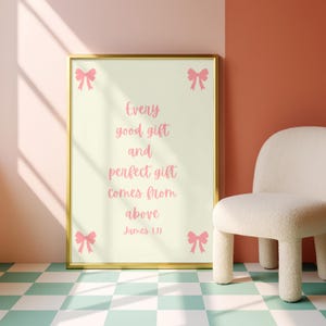 Könnte beinhalten: Ein gerahmter Druck mit goldenem Rahmen zeigt den Text "Every good gift and perfect gift comes from above James 1:17" in rosa Schrift. Rosa Schleifen-Illustrationen befinden sich in jeder Ecke. Rechts steht ein weißer Stuhl mit abgerundeten Beinen.