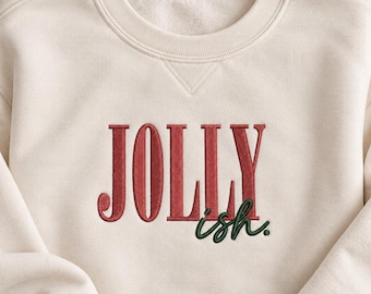 May include: A cream-colored crewneck sweatshirt featuring embroidered text on the chest. The word JOLLY is stitched in red capital letters, with the word ish. embroidered in dark green lowercase script letters positioned below the right side.