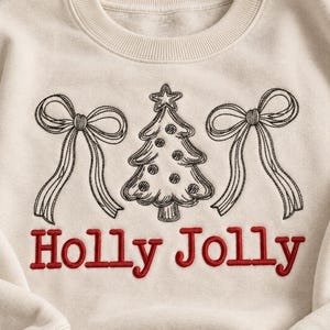 May include: A cream-colored crewneck sweatshirt featuring black embroidered line art of a Christmas tree flanked by two bows. Below the design, the text "Holly Jolly" is embroidered in red thread with a classic serif font style.