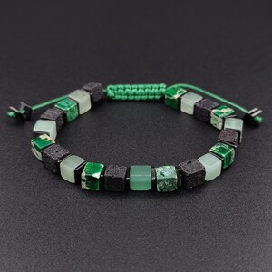 May include: A green and black cube bead bracelet. The bracelet features square beads in shades of green and black, strung together with a green cord. The adjustable bracelet is approximately 7 inches in length.