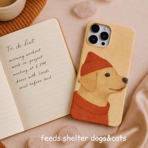 May include: A beige phone case with a watercolour illustration of a golden retriever wearing a red hat and sweater. A notebook with a to-do list and the text "feeds shelter dogs&cats" are also visible.