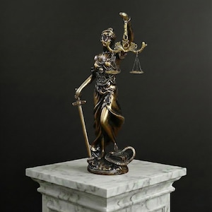 May include: A bronze-colored statue of Lady Justice, holding scales and a sword, stands on a marble pedestal. The statue features a blindfold and a serpent at its base, symbolizing justice and law.