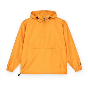 May include: A bright orange anorak jacket with a hood and a half-zip closure. The jacket has long sleeves, a front pocket, and a small logo on the left sleeve. The drawstring hood and hem allow for an adjustable fit.