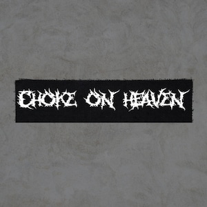 May include: Black rectangular patch with the text "CHOKE ON HEAVEN" in white, stylized, spiky font. The patch has a rough, textured appearance, suggesting a fabric material. The background is a plain, light gray surface.