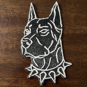 May include: Black and white dog head silhouette. The dog's head is in profile, with a spiked collar. The design is a bold, graphic illustration, perfect for dog lovers. The dog's features are outlined in white against a black background.
