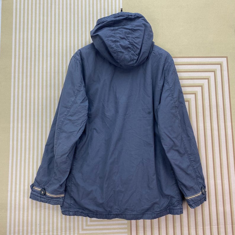 May include: A blue hooded jacket with a full zipper closure. The jacket has a drawstring hood, long sleeves, and a straight hemline. The cuffs have a white and yellow stripe detail. The jacket is made of a lightweight material.