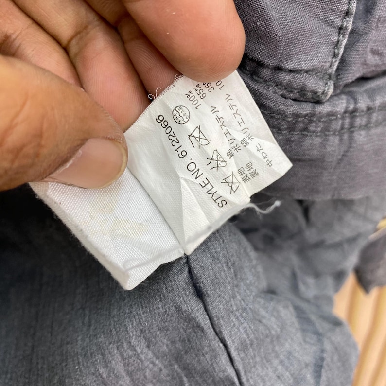 May include: Close-up of a gray garment tag with the text "STYLE NO. 6122066". The tag also includes washing instructions and fabric composition details, including percentages of polyester and cotton.